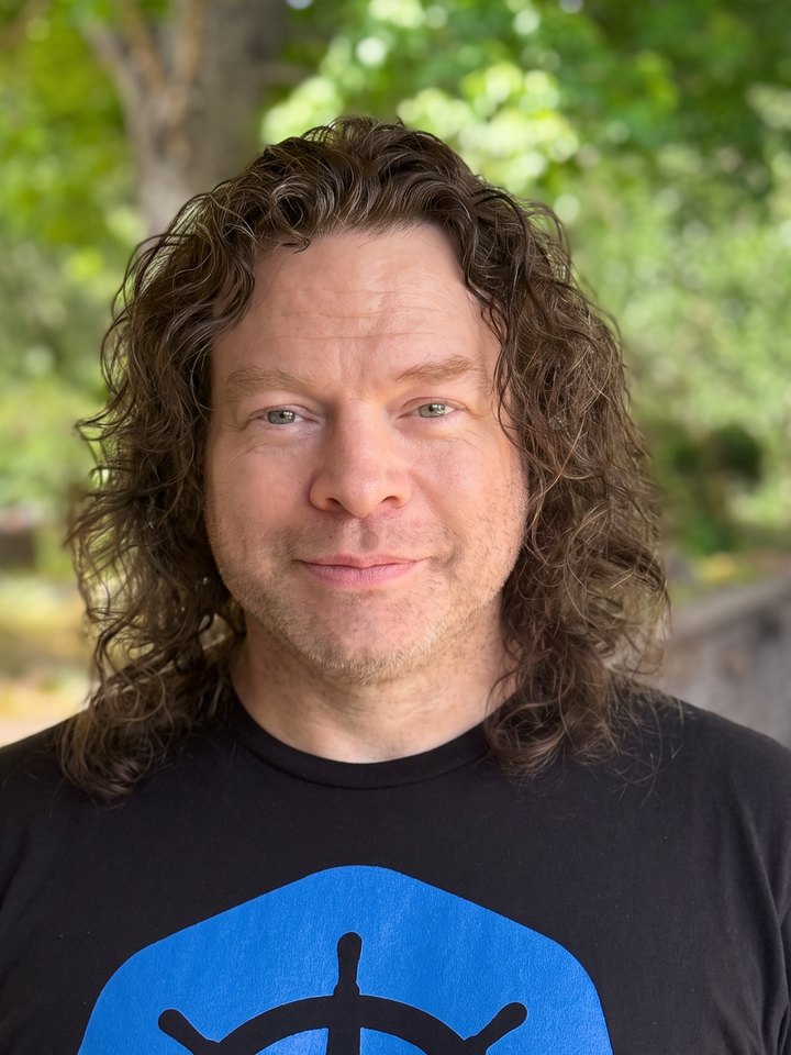 Alec, face forward and smiling, outdoors under green trees.