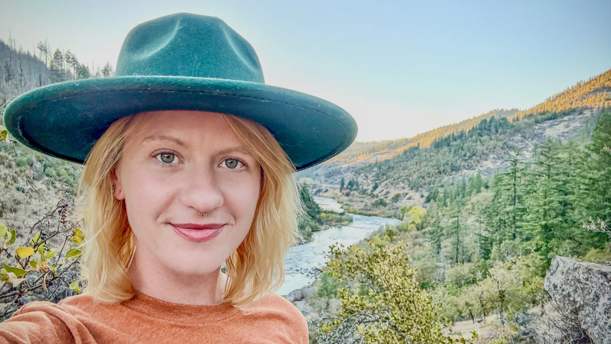 Sasha smiling in her green hat, the river winding through a golden canyon behind her